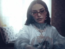 a woman wearing sunglasses and a necklace has a white shirt with a picture of a horse on it
