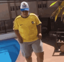 a man wearing a yellow nike shirt and a white hat is standing next to a pool