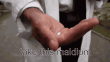 a man in a lab coat is holding a small white pill in his hand with the words take this maldium written below it