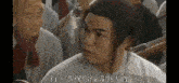 a man with long hair is sitting in a crowd of people and talking to another man .