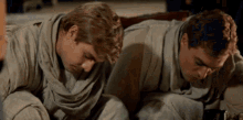 two men are laying on the floor with their heads together .
