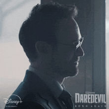 a poster for daredevil born again shows a man in a suit and tie looking out a window