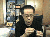 a man wearing glasses is sitting in front of a bookshelf with a yellow bag that says lucky
