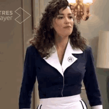 a woman with curly hair is wearing a maid 's uniform and standing in a room .