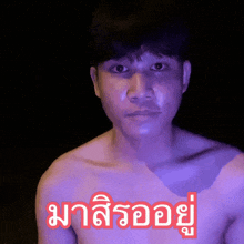 a man without a shirt is standing in front of a sign that says ' มา ลิ รอ อยู่ '
