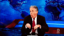 a man in a suit and tie is sitting in front of a comedy talk show