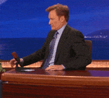 a man in a suit is sitting at a desk with his hands up