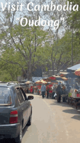 a car is parked on the side of the road in front of a market called oudong in cambodia
