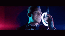 a man in a tuxedo is singing into a microphone in front of a light circle