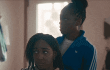 a woman in a blue adidas jacket is combing the hair of another woman