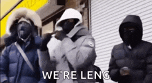 a group of people wearing hooded jackets and masks are standing next to each other in front of a building .