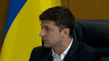 a man in a suit sitting in front of a flag