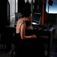 a woman in a black dress is standing in a room with clothes hanging on a rack and a table