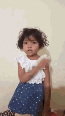 a little girl wearing a white top and blue skirt