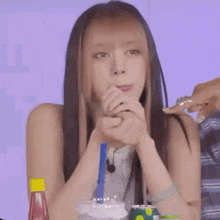a woman with long hair is sitting at a table with a drink in her hand and looking at the camera .
