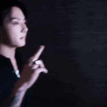 a man with a ring on his finger is standing in the dark and pointing at something .