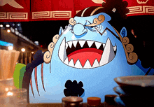 a cartoon character with a huge mouth and sharp teeth is sitting on a table