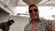 a man wearing sunglasses and a hawaiian shirt is smiling in front of a man wearing a mask