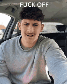 a man sitting in a car with the words fuck off written above him
