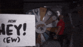 a man in a red shirt stands in front of a spinning wheel with a sign that says hey