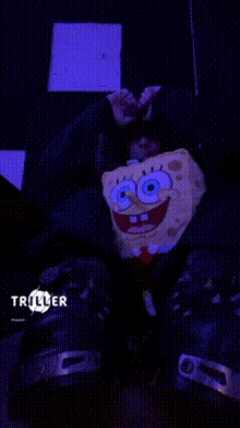 a spongebob stuffed animal is sitting in a dark room with a triller logo in the corner