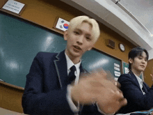 two boys in suits are clapping in front of a blackboard