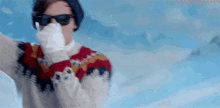 a man wearing a sweater , sunglasses , and gloves is standing in the snow .
