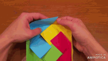 a person is holding a colorful origami cube that is made in animatica