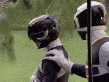 two power rangers are standing next to each other and one of them is touching the other 's shoulder .