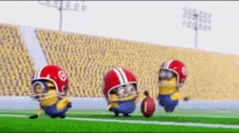 three minions wearing helmets and holding a football on a football field .