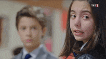 a girl making a funny face in front of a boy in a suit and tie with trt 1 written on the bottom right