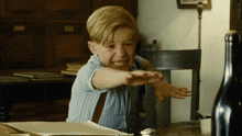 a young boy is sitting at a table with his hand outstretched
