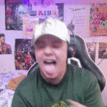 a man wearing headphones and a hat is sticking his tongue out in front of a wall with posters on it