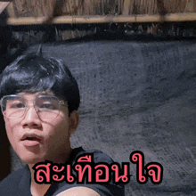 a man wearing glasses and a black shirt has a foreign language written on his chest
