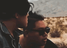a couple of men wearing sunglasses are sitting next to each other in the desert .