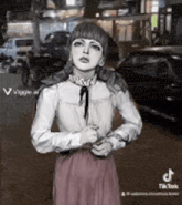 a woman in a white shirt and pink skirt is standing in front of a street .