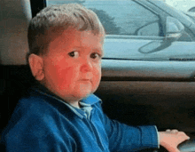 a young boy with red spots on his face is sitting in a car and looking out the window .