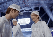 a man wearing a white baseball cap talks to another man