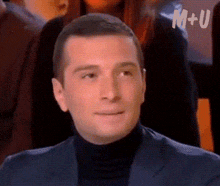 a man in a suit and black turtleneck is smiling in front of a m + u logo ..