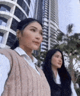 two women standing next to each other in front of a tall building .