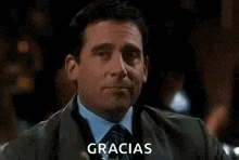 a man in a suit and tie is holding a glass of whiskey and saying gracias .
