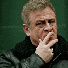 a man wearing a black jacket holds his finger to his chin