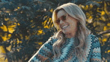 a woman wearing sunglasses and a patterned shirt smiles for the camera