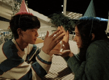 a man and a woman wearing party hats are giving each other a high five