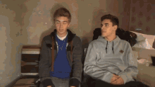 two boys sitting next to each other with one wearing a grey sweatshirt