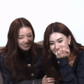 two women are sitting next to each other on a couch and one is covering her mouth with her hand