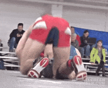 a couple of men are wrestling on a wrestling mat in front of a crowd .