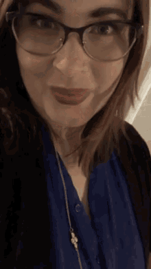 a woman wearing glasses and a blue shirt is taking a selfie