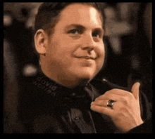 a man wearing a black shirt and bow tie is giving a thumbs up by david warren