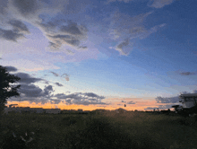 a sunset over a field with a few clouds in the sky